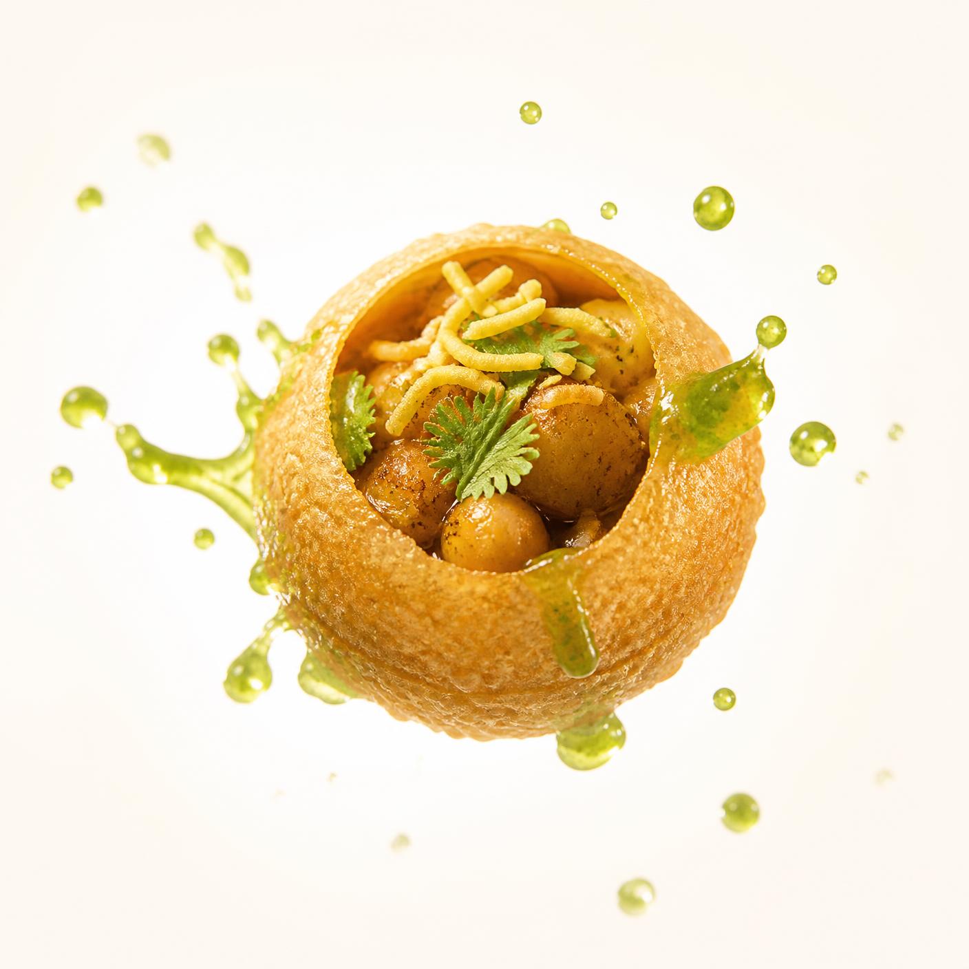 A crisp pani puri filled with potato, chana and sev with mint pani splashing around it